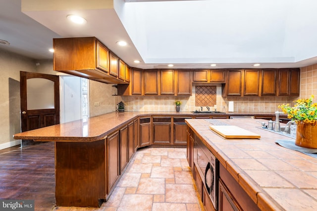 kitchen with tile countertops, stainless steel microwave, sink, tasteful backsplash, and a tray ceiling