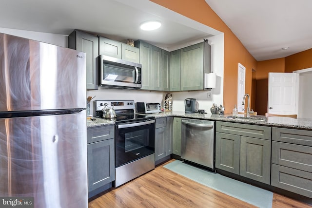 kitchen featuring light stone countertops, appliances with stainless steel finishes, light wood-type flooring, and sink