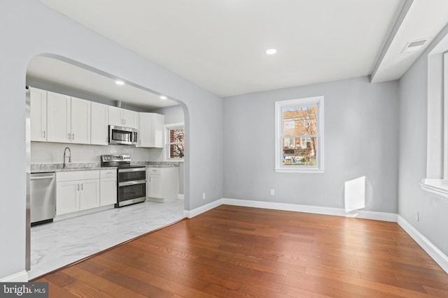 kitchen with backsplash, white cabinets, light wood-type flooring, light stone countertops, and stainless steel appliances