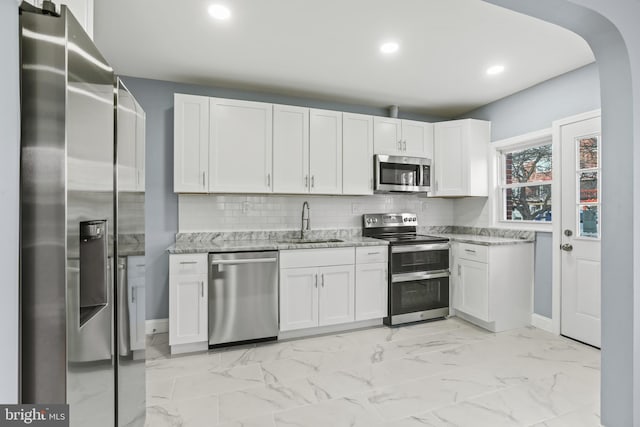 kitchen featuring white cabinetry, sink, light stone countertops, tasteful backsplash, and appliances with stainless steel finishes