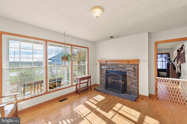 living room featuring light hardwood / wood-style floors, a stone fireplace, a textured ceiling, and a wealth of natural light