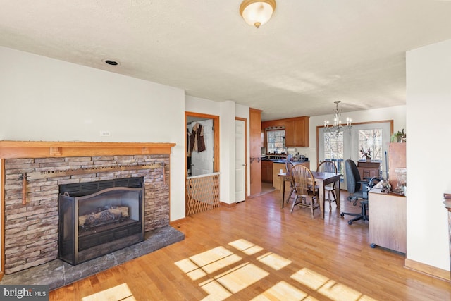 living room featuring a chandelier, a textured ceiling, light hardwood / wood-style flooring, and a stone fireplace