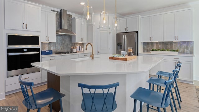 kitchen featuring white cabinetry, a kitchen bar, wall chimney range hood, and appliances with stainless steel finishes