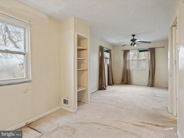 carpeted spare room with a textured ceiling, plenty of natural light, and ceiling fan