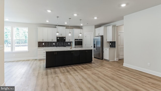 kitchen with appliances with stainless steel finishes, light wood-type flooring, a kitchen island with sink, white cabinets, and hanging light fixtures