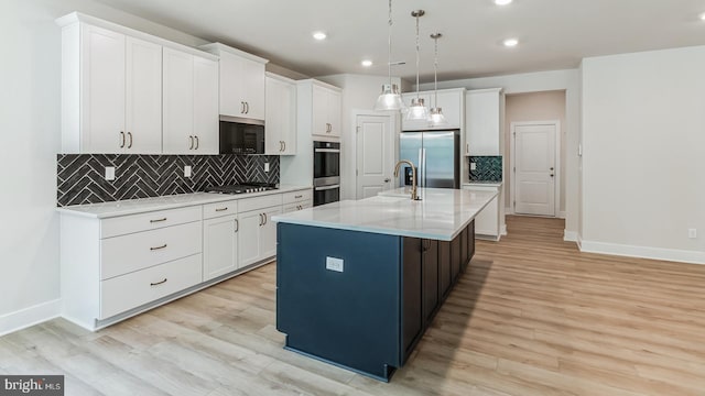 kitchen with a center island with sink, white cabinetry, stainless steel appliances, and hanging light fixtures