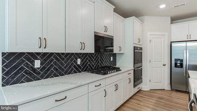 kitchen featuring white cabinets, light hardwood / wood-style flooring, decorative backsplash, appliances with stainless steel finishes, and light stone counters