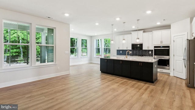 kitchen featuring pendant lighting, decorative backsplash, an island with sink, appliances with stainless steel finishes, and light hardwood / wood-style floors