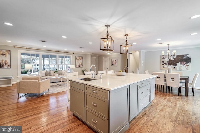 kitchen with sink, an island with sink, hanging light fixtures, and light wood-type flooring