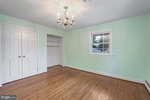 unfurnished bedroom with a chandelier, hardwood / wood-style floors, and a baseboard heating unit