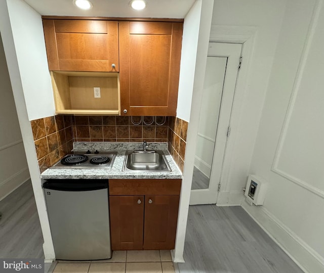 kitchen with decorative backsplash, light wood-type flooring, stainless steel dishwasher, electric stovetop, and sink