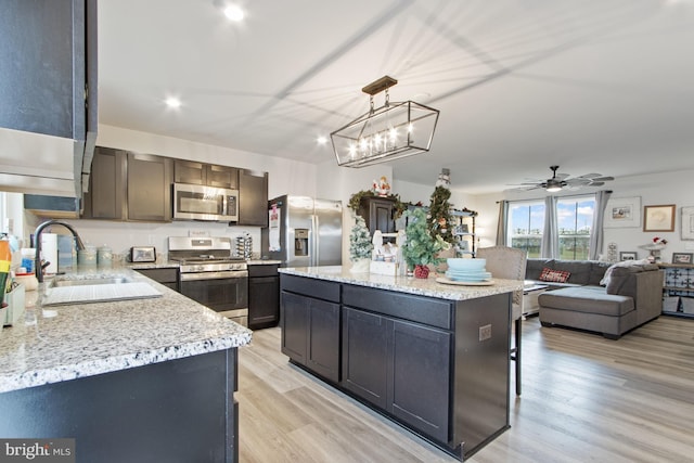 kitchen featuring appliances with stainless steel finishes, sink, decorative light fixtures, light hardwood / wood-style floors, and a kitchen island