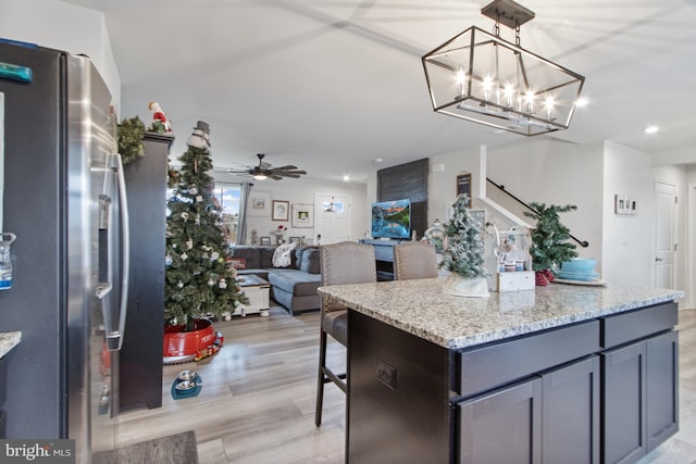 kitchen featuring light stone countertops, stainless steel fridge, ceiling fan with notable chandelier, decorative light fixtures, and light hardwood / wood-style flooring