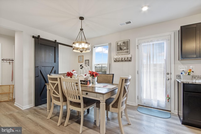 dining room with a barn door, a wealth of natural light, light hardwood / wood-style floors, and a notable chandelier