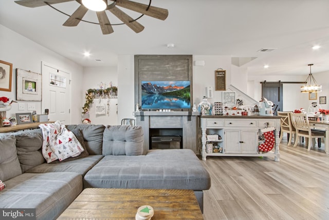 living room featuring a fireplace, a barn door, light hardwood / wood-style flooring, and ceiling fan