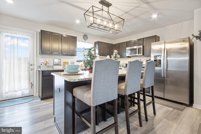 kitchen featuring dark brown cabinetry, a center island, stainless steel appliances, pendant lighting, and light hardwood / wood-style floors