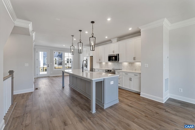 kitchen with white cabinetry, an island with sink, pendant lighting, wood-type flooring, and appliances with stainless steel finishes