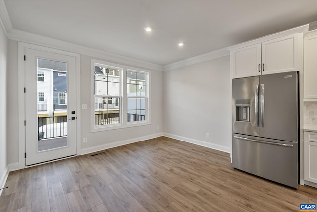 kitchen with stainless steel fridge with ice dispenser, light hardwood / wood-style flooring, white cabinetry, and ornamental molding