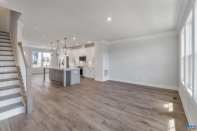 kitchen featuring white cabinetry, an island with sink, light hardwood / wood-style floors, pendant lighting, and appliances with stainless steel finishes