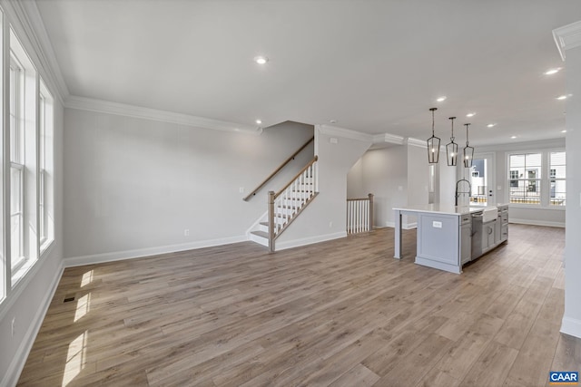 kitchen featuring a kitchen bar, crown molding, pendant lighting, light hardwood / wood-style floors, and an island with sink