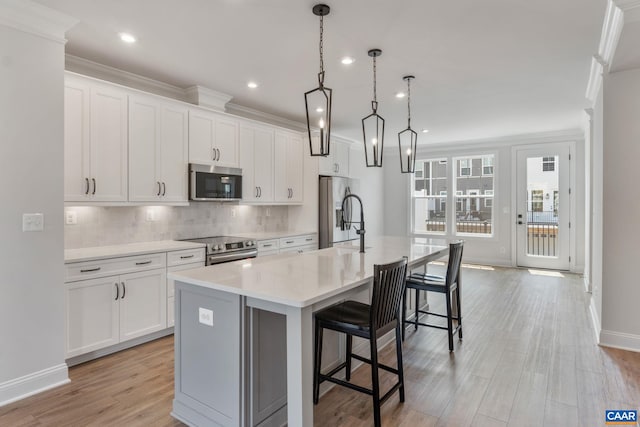 kitchen with white cabinetry, stainless steel appliances, an island with sink, decorative light fixtures, and a breakfast bar area