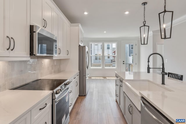 kitchen featuring light hardwood / wood-style flooring, ornamental molding, appliances with stainless steel finishes, tasteful backsplash, and white cabinetry