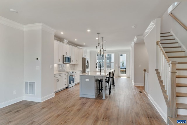 kitchen featuring hanging light fixtures, light hardwood / wood-style flooring, a center island with sink, white cabinets, and appliances with stainless steel finishes