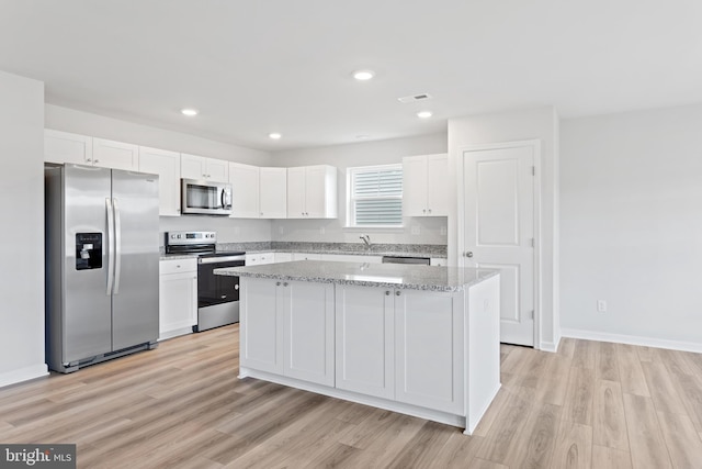 kitchen with white cabinetry, stainless steel appliances, light stone counters, light hardwood / wood-style floors, and a kitchen island