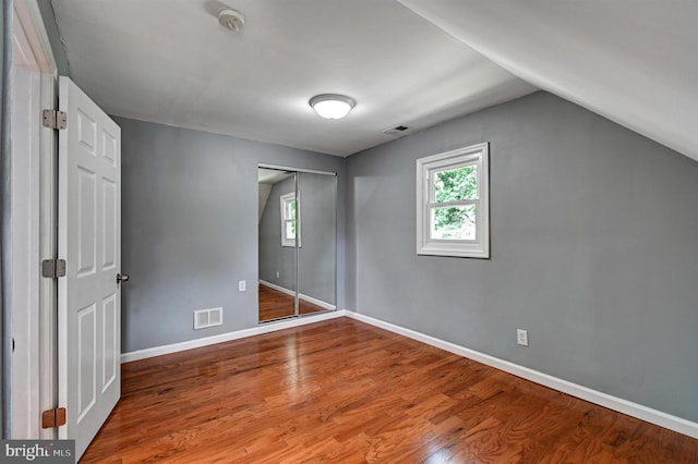 unfurnished bedroom featuring a closet, wood-type flooring, and lofted ceiling