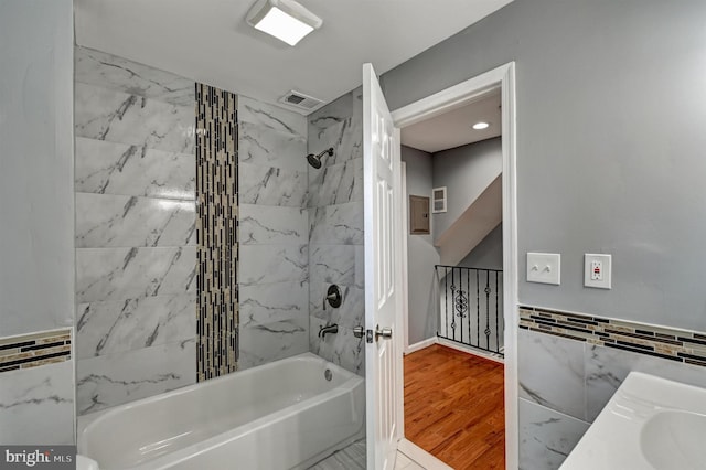 bathroom featuring hardwood / wood-style floors, vanity, tiled shower / bath, and tile walls