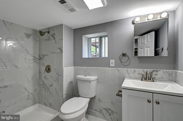 bathroom featuring vanity, toilet, tile walls, and a tile shower