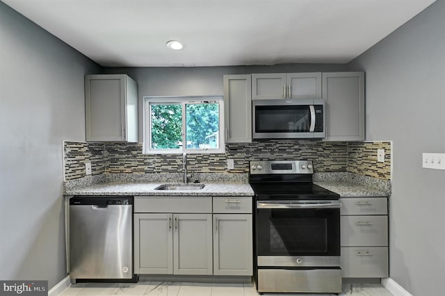 kitchen featuring tasteful backsplash, light stone counters, sink, and stainless steel appliances