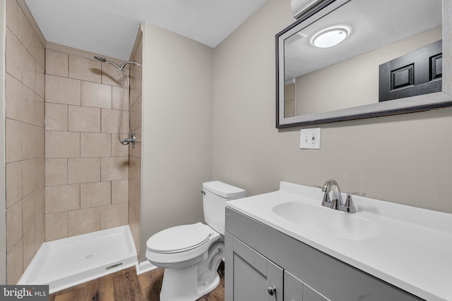 bathroom featuring hardwood / wood-style floors, vanity, toilet, and a tile shower