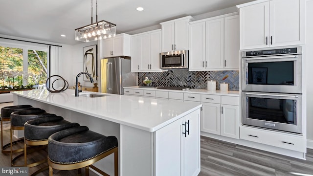 kitchen featuring appliances with stainless steel finishes, sink, a center island with sink, white cabinets, and hanging light fixtures