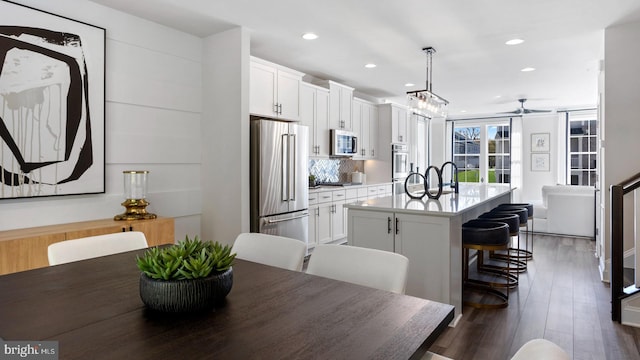 kitchen with pendant lighting, white cabinets, an island with sink, appliances with stainless steel finishes, and dark hardwood / wood-style flooring