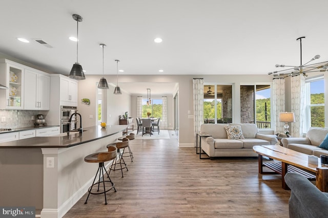 kitchen with tasteful backsplash, decorative light fixtures, a breakfast bar, white cabinets, and hardwood / wood-style flooring