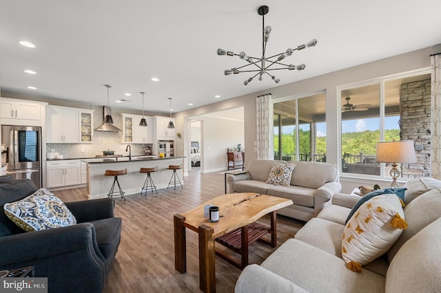 living room with sink, ceiling fan with notable chandelier, and light wood-type flooring