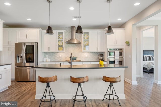 kitchen with white cabinets, wall chimney range hood, a breakfast bar area, and appliances with stainless steel finishes