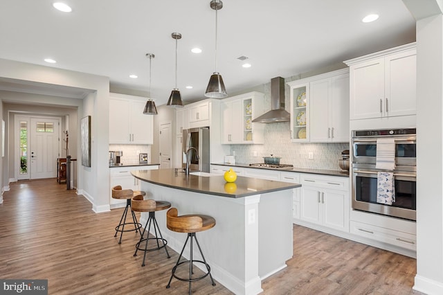 kitchen featuring appliances with stainless steel finishes, white cabinetry, hanging light fixtures, and wall chimney range hood