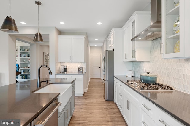 kitchen with wall chimney exhaust hood, stainless steel appliances, sink, decorative light fixtures, and white cabinetry