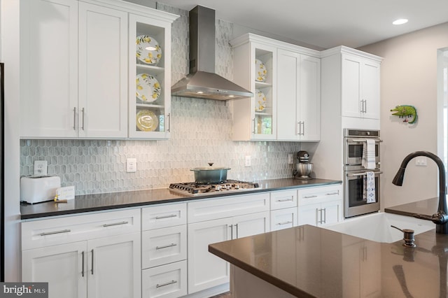 kitchen with white cabinets, sink, stainless steel appliances, and wall chimney range hood