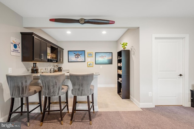 bar with dark brown cabinets, sink, and light carpet