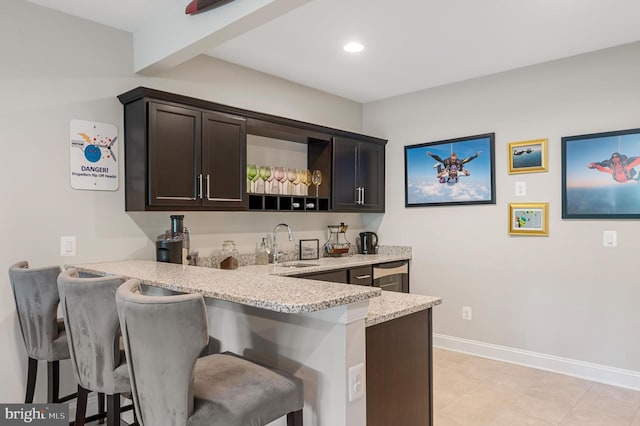 bar with light stone countertops, sink, and dark brown cabinets