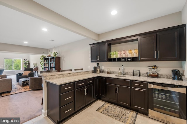 kitchen with kitchen peninsula, light stone counters, beverage cooler, and sink