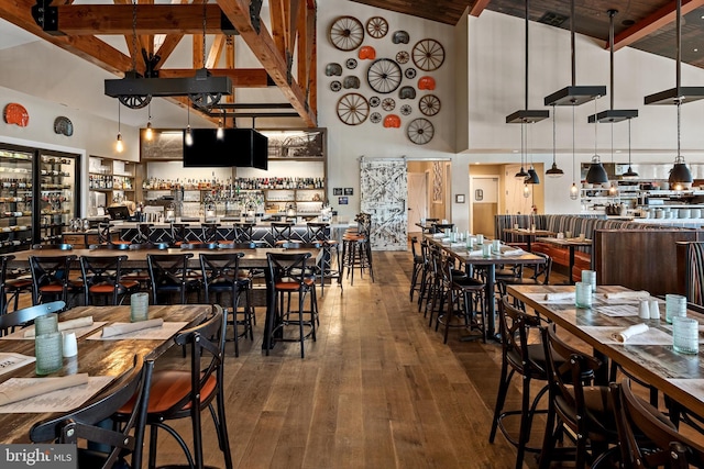 dining area with beam ceiling, hardwood / wood-style floors, high vaulted ceiling, and indoor bar