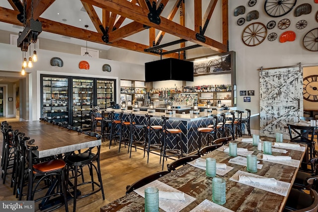 dining area featuring beam ceiling, hardwood / wood-style flooring, high vaulted ceiling, and bar