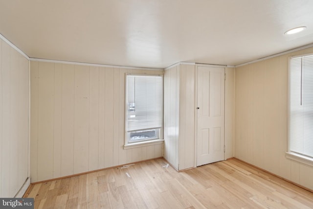 unfurnished bedroom with ornamental molding, light wood-type flooring, and wooden walls