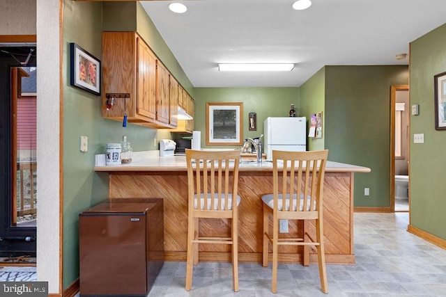 kitchen featuring kitchen peninsula, a kitchen breakfast bar, and white appliances