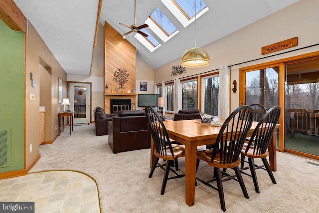 dining space featuring light carpet, high vaulted ceiling, a skylight, ceiling fan, and a fireplace