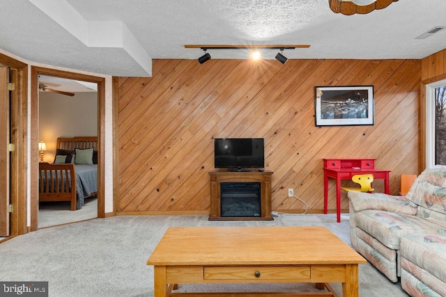 carpeted living room featuring ceiling fan, a textured ceiling, wooden walls, and track lighting